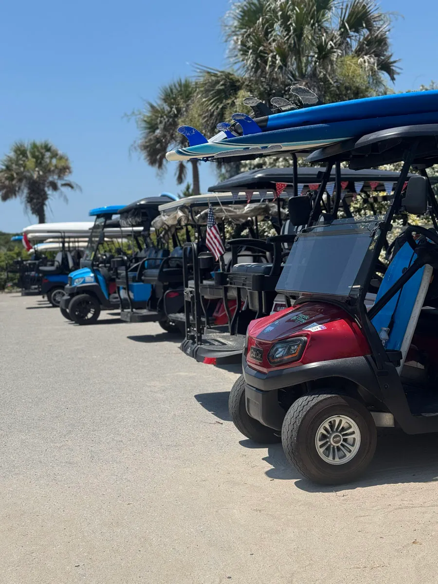 A row of golf carts loaded with surfboards near the beach