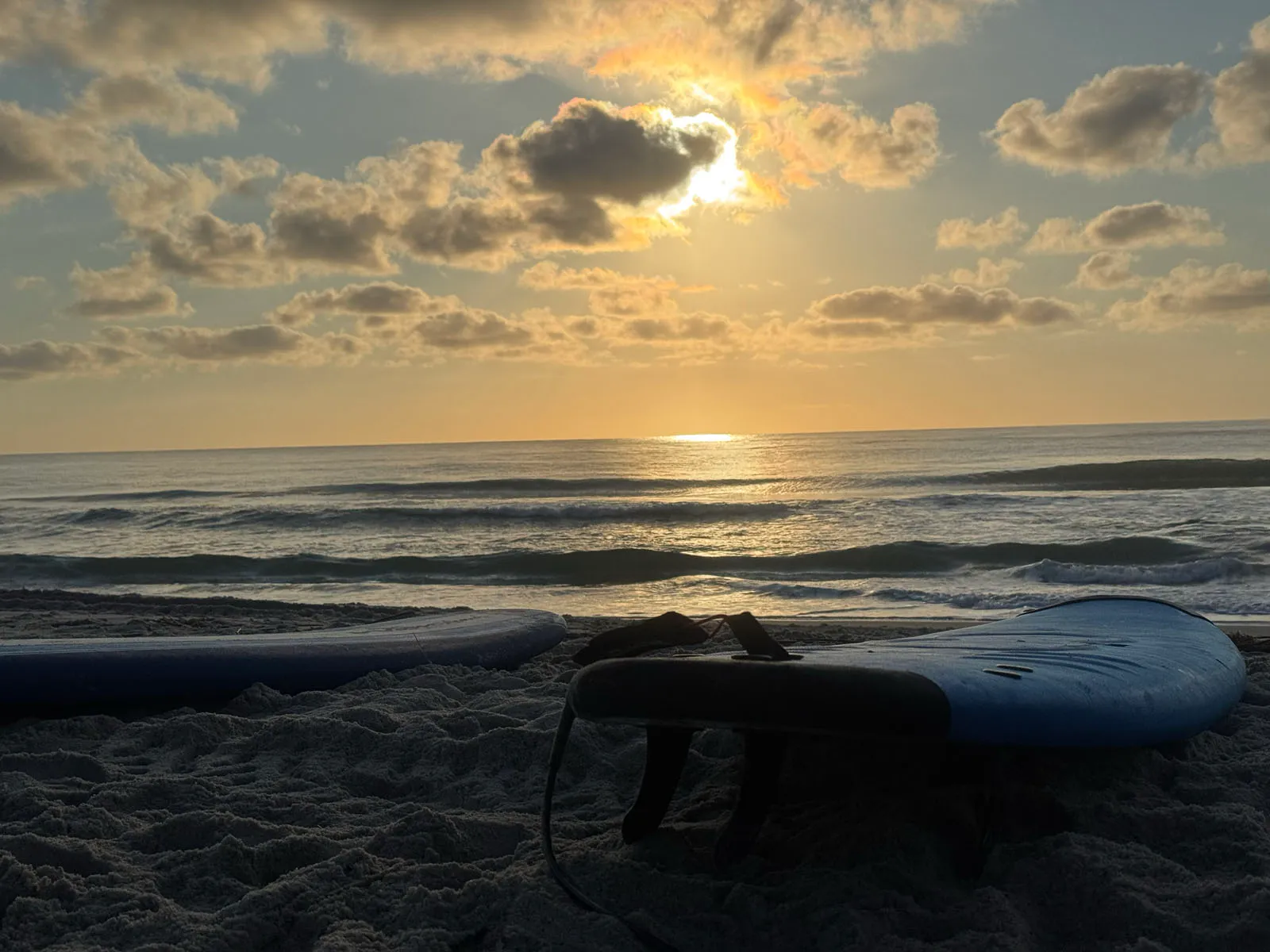 Sunrise over the ocean with surfboards resting on the beach in the foreground